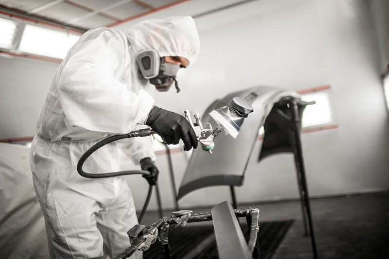 A person in full protective gear painting a car part